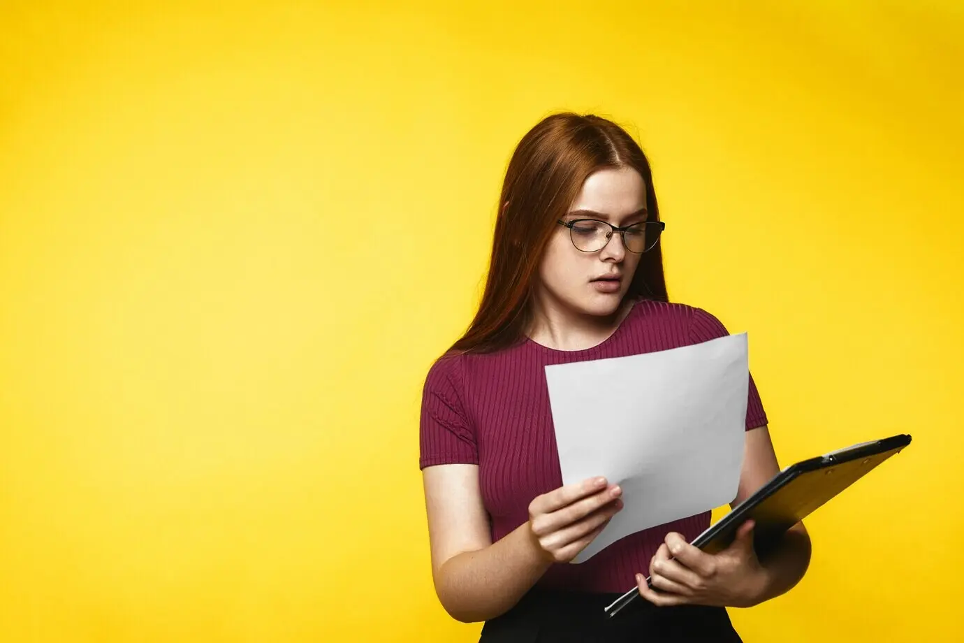 Ein junges rothaariges Mädchen blickt in die Dokumente und hat einen ernsten Gesichtsausdruck.
